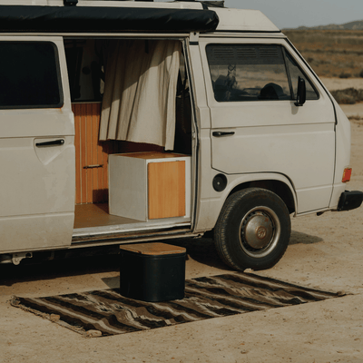 A Trelino Origin M composting toilet serves as a step into a van, which is parked alone on a serene beach.