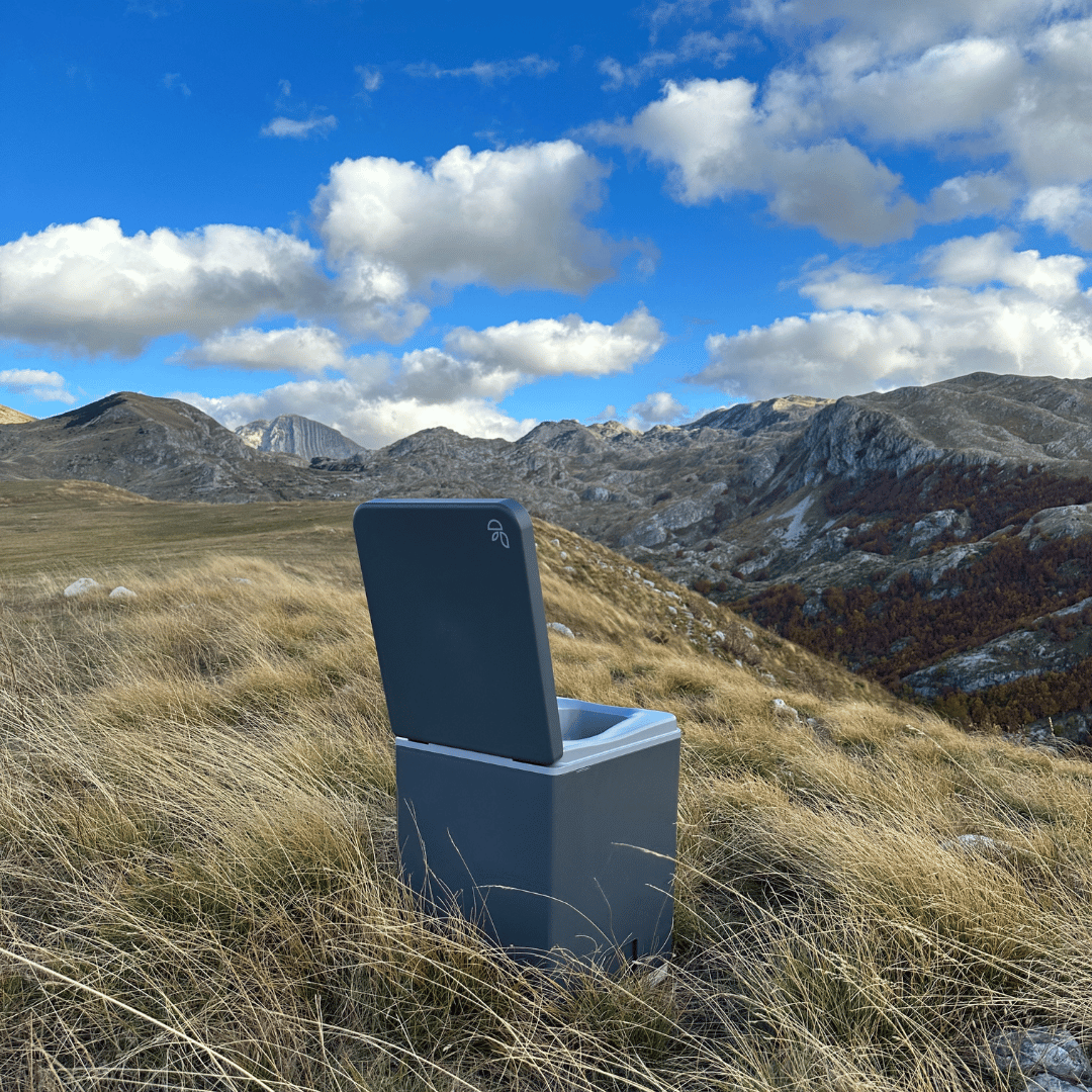 Evo L composting toilet in a meadow with a view of the mountains, far from civilization, surrounded by untouched nature.