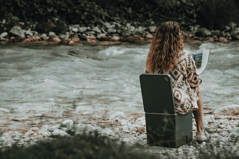 Person reading by a river on a composting toilet