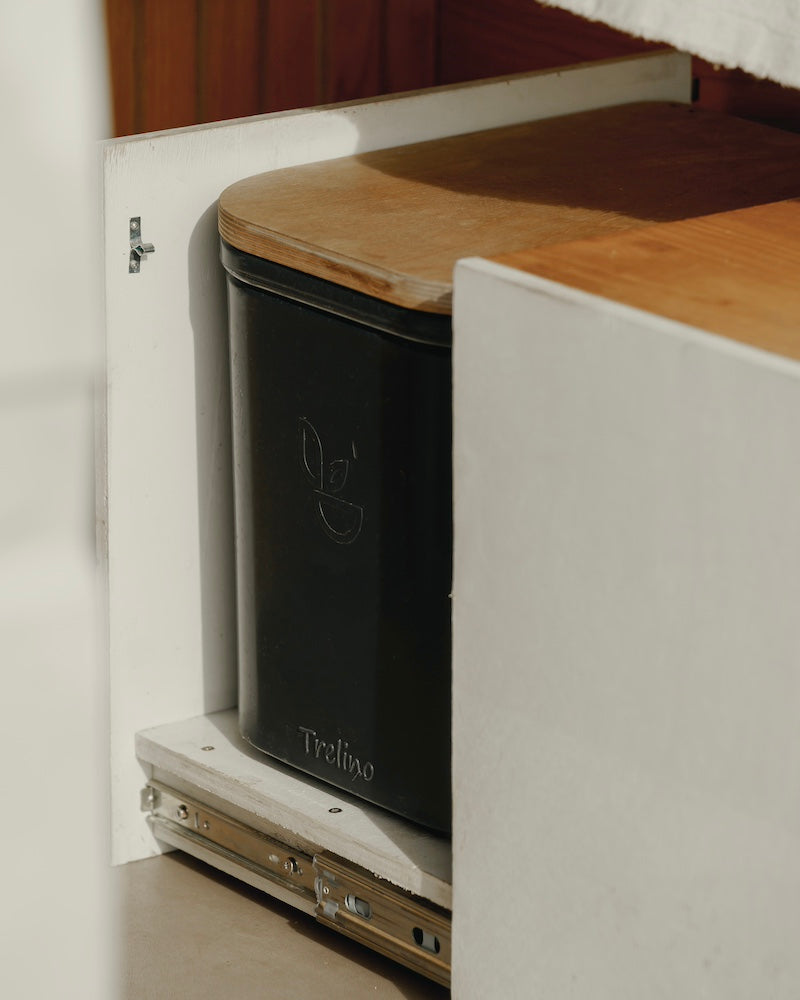 Black camping toilet with wooden lid inside a cabinet, featuring the Treeline brand logo.